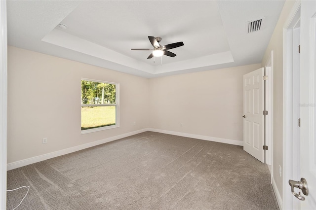 empty room with a raised ceiling, ceiling fan, and carpet flooring