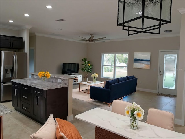 interior space featuring stainless steel refrigerator with ice dispenser, crown molding, light tile patterned floors, a kitchen island, and light stone countertops