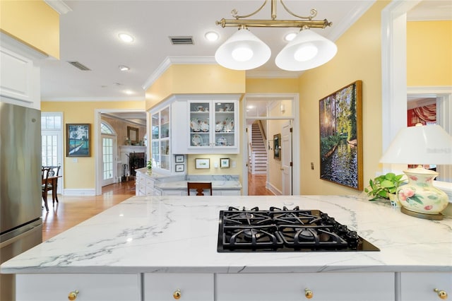 kitchen with white cabinetry, stainless steel fridge, hanging light fixtures, light stone counters, and black gas stovetop