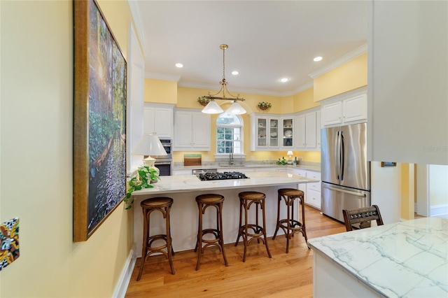 kitchen with appliances with stainless steel finishes, white cabinets, a kitchen breakfast bar, hanging light fixtures, and crown molding