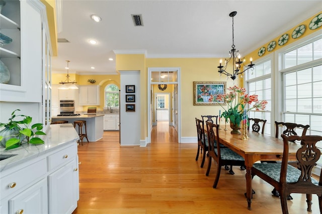 dining area featuring an inviting chandelier, light hardwood / wood-style flooring, ornamental molding, and a healthy amount of sunlight