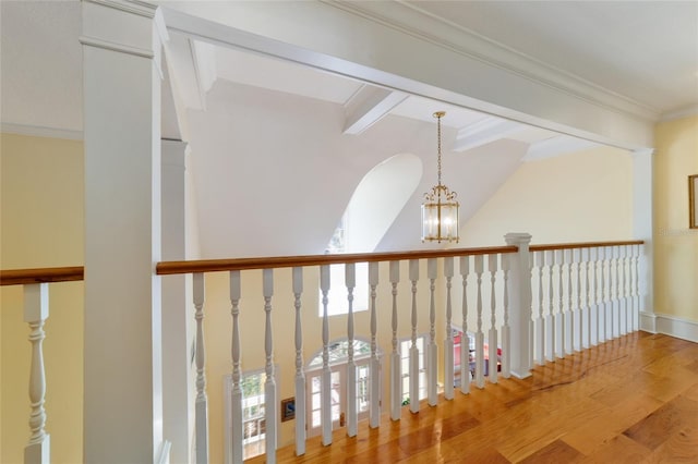 hall featuring ornate columns, beamed ceiling, wood-type flooring, a chandelier, and ornamental molding