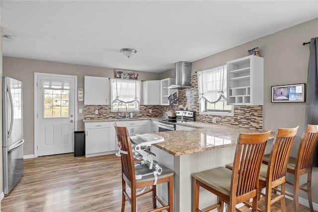 kitchen with appliances with stainless steel finishes, a breakfast bar, white cabinetry, kitchen peninsula, and wall chimney exhaust hood