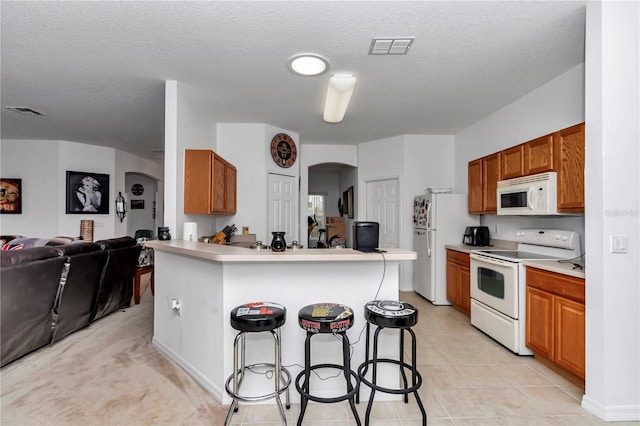 kitchen with light tile patterned floors, white appliances, a textured ceiling, a kitchen bar, and kitchen peninsula