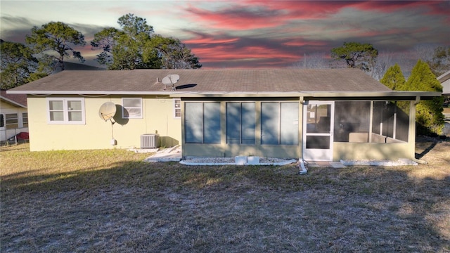 back house at dusk with central AC, a lawn, and a sunroom