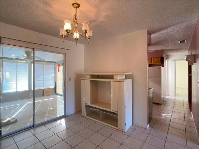 interior space featuring ceiling fan with notable chandelier, white refrigerator, hanging light fixtures, light tile patterned floors, and a textured ceiling