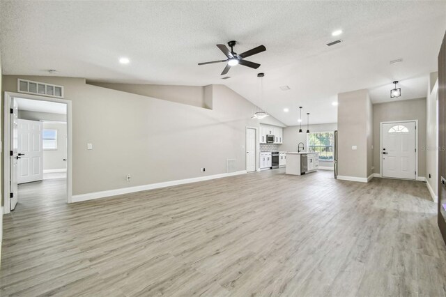 unfurnished living room with vaulted ceiling, light wood-style flooring, a sink, and visible vents