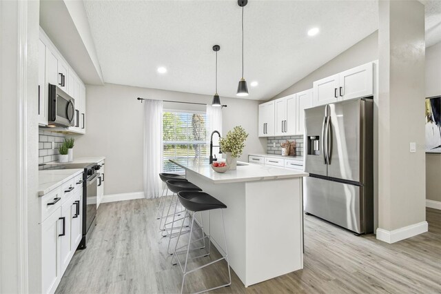 kitchen with pendant lighting, appliances with stainless steel finishes, white cabinetry, a sink, and an island with sink