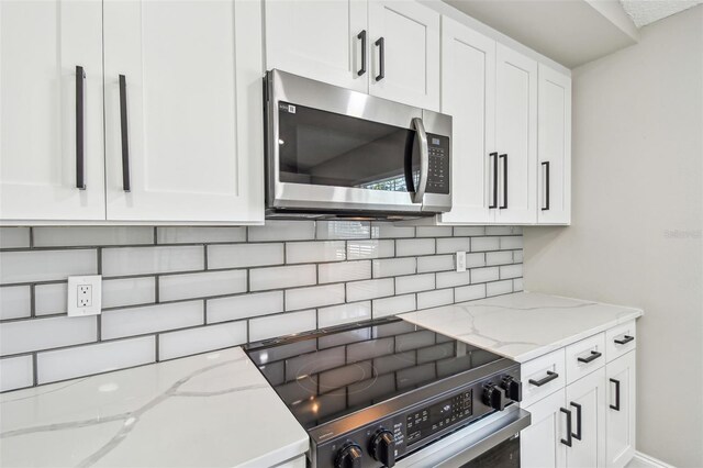 kitchen with stainless steel appliances, white cabinets, decorative backsplash, and light stone countertops