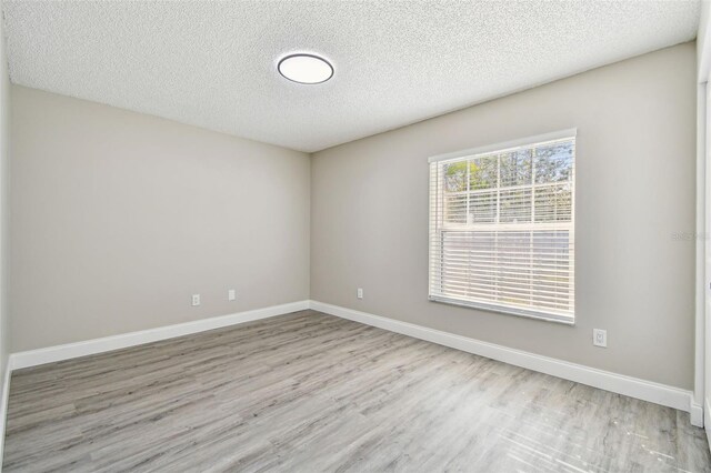 empty room with a textured ceiling, light wood finished floors, and baseboards