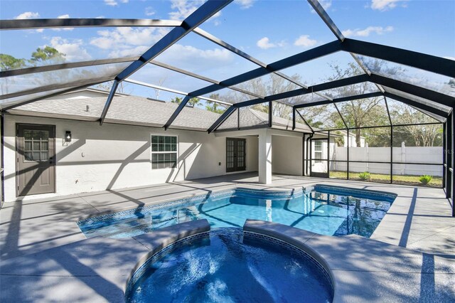 view of pool with glass enclosure, a pool with connected hot tub, a patio area, and fence