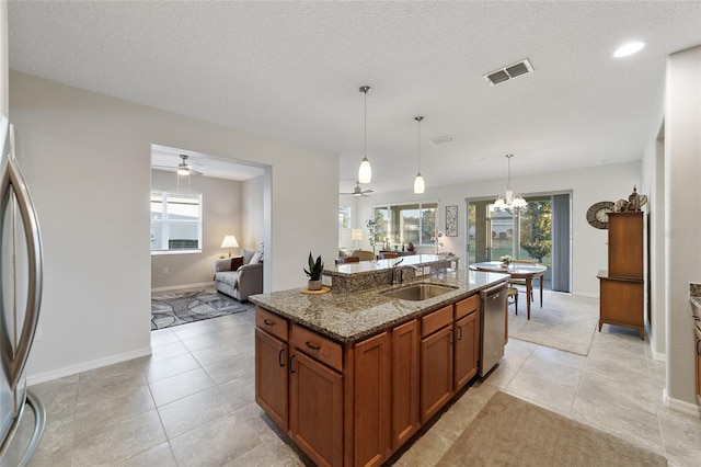 kitchen with sink, dark stone countertops, hanging light fixtures, stainless steel appliances, and an island with sink