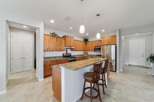 kitchen featuring a center island with sink, appliances with stainless steel finishes, a kitchen breakfast bar, stone counters, and pendant lighting