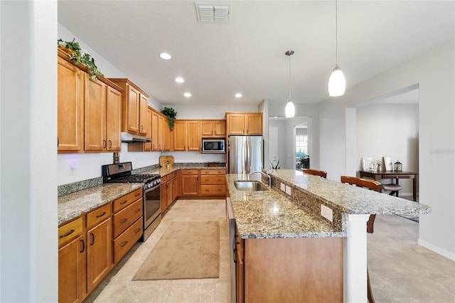 kitchen with appliances with stainless steel finishes, decorative light fixtures, an island with sink, sink, and a kitchen breakfast bar