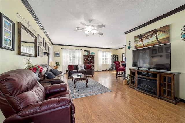 living room featuring ornamental molding, wood-type flooring, ceiling fan, and a textured ceiling