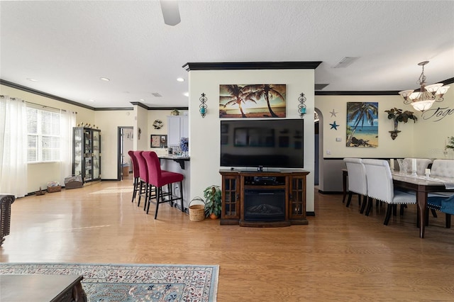 living room with crown molding, an inviting chandelier, light hardwood / wood-style flooring, and a textured ceiling