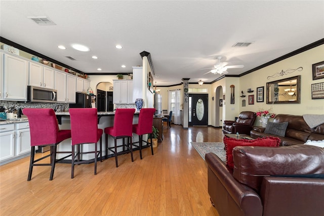 kitchen featuring a kitchen bar, black fridge, crown molding, light hardwood / wood-style flooring, and white cabinets