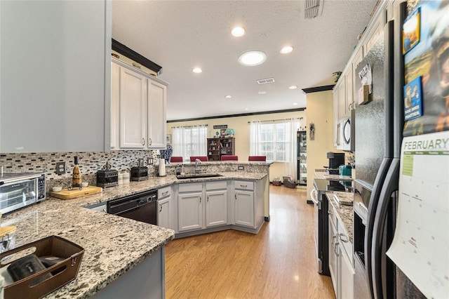 kitchen featuring sink, white cabinetry, light stone counters, kitchen peninsula, and black appliances