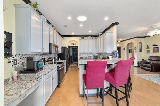 kitchen featuring stainless steel appliances, a breakfast bar, white cabinets, and light stone counters