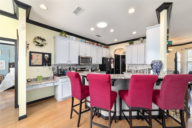 kitchen featuring white cabinetry, ornamental molding, appliances with stainless steel finishes, a kitchen breakfast bar, and light stone countertops