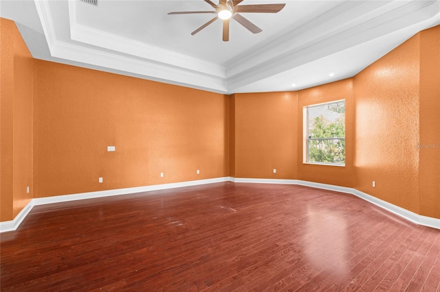 empty room with ceiling fan, wood-type flooring, a tray ceiling, and ornamental molding