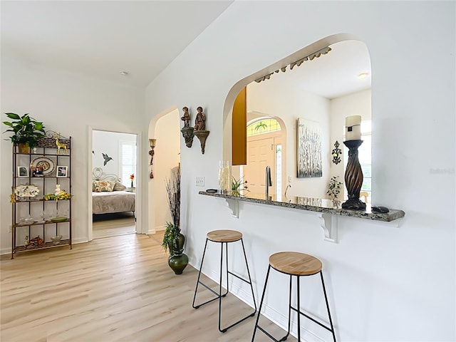 kitchen with a kitchen bar, kitchen peninsula, light wood-type flooring, and dark stone countertops