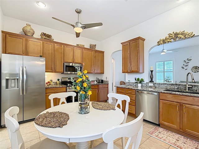 kitchen with sink, light tile patterned floors, ceiling fan, stainless steel appliances, and stone countertops