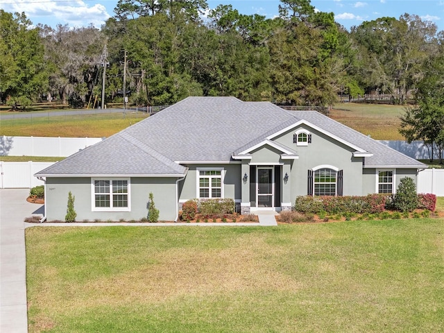 ranch-style home featuring a shingled roof, a front yard, and fence