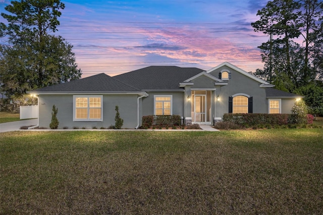 ranch-style house with stucco siding, a shingled roof, and a front lawn