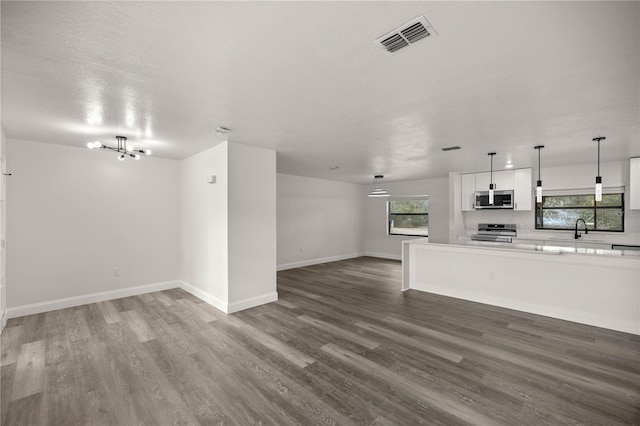 unfurnished living room featuring an inviting chandelier, sink, hardwood / wood-style floors, and a textured ceiling