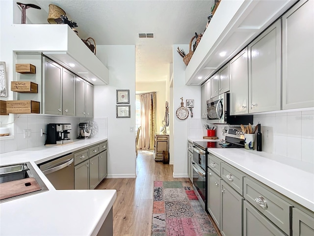 kitchen featuring appliances with stainless steel finishes, gray cabinets, light hardwood / wood-style floors, and backsplash