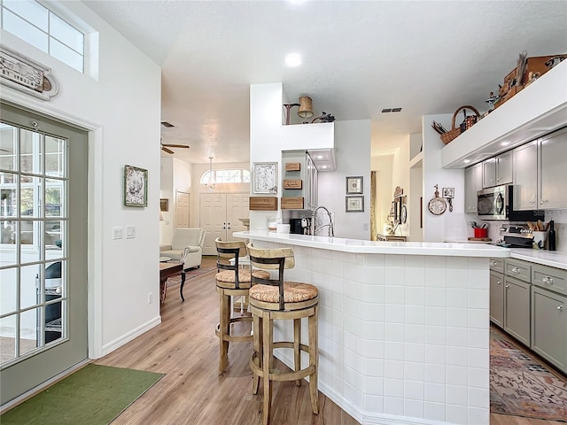 kitchen featuring a breakfast bar, ceiling fan, gray cabinetry, an island with sink, and light wood-type flooring