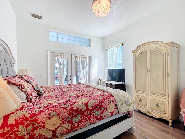 bedroom with access to outside, light hardwood / wood-style floors, french doors, and a textured ceiling