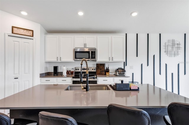 kitchen featuring sink, appliances with stainless steel finishes, white cabinetry, a kitchen breakfast bar, and an island with sink