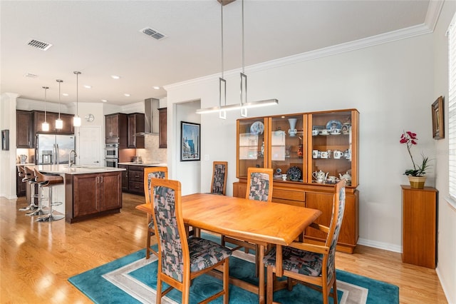 dining area with sink, crown molding, and light hardwood / wood-style flooring