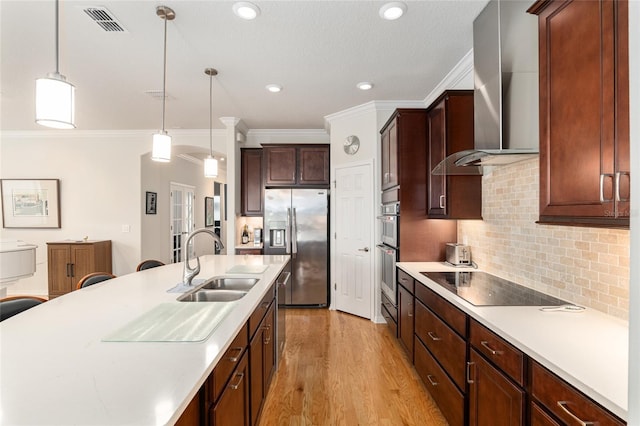 kitchen with appliances with stainless steel finishes, sink, hanging light fixtures, and wall chimney range hood