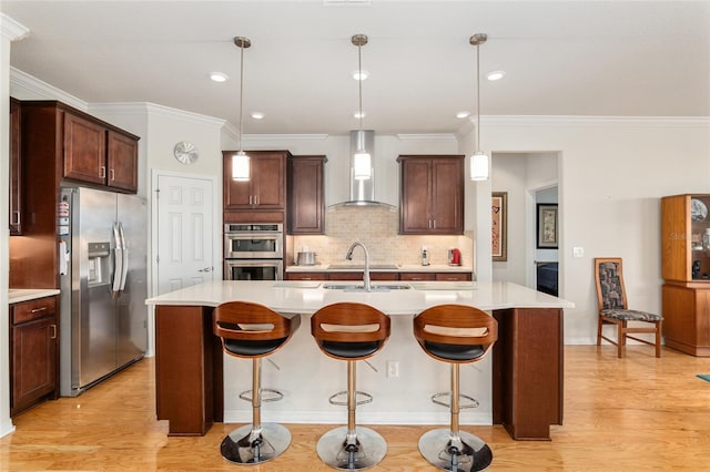 kitchen featuring decorative light fixtures, a center island with sink, wall chimney exhaust hood, and appliances with stainless steel finishes