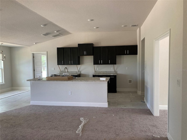 kitchen featuring vaulted ceiling, a kitchen island, light colored carpet, a textured ceiling, and an inviting chandelier