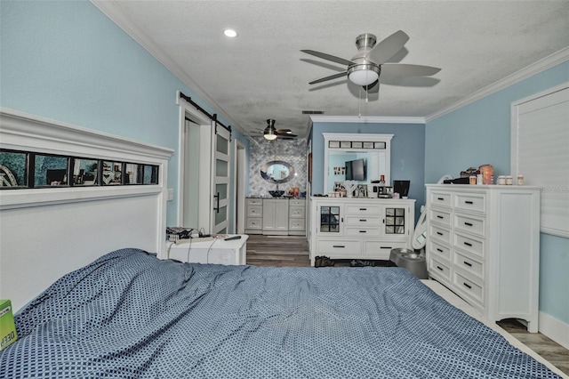bedroom with a textured ceiling, a barn door, wood finished floors, and crown molding
