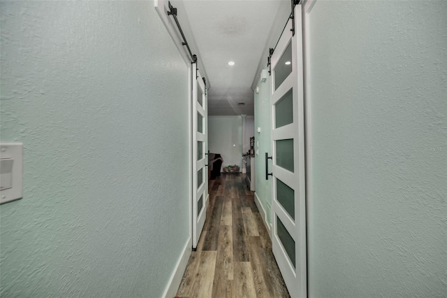 hallway featuring a barn door, wood finished floors, and a textured wall