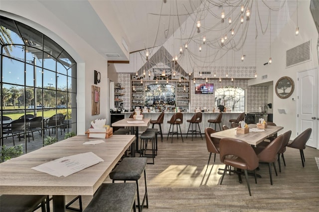 dining space featuring a community bar, visible vents, a towering ceiling, wood finished floors, and an inviting chandelier