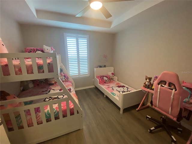 bedroom featuring a ceiling fan, a tray ceiling, baseboards, and wood finished floors