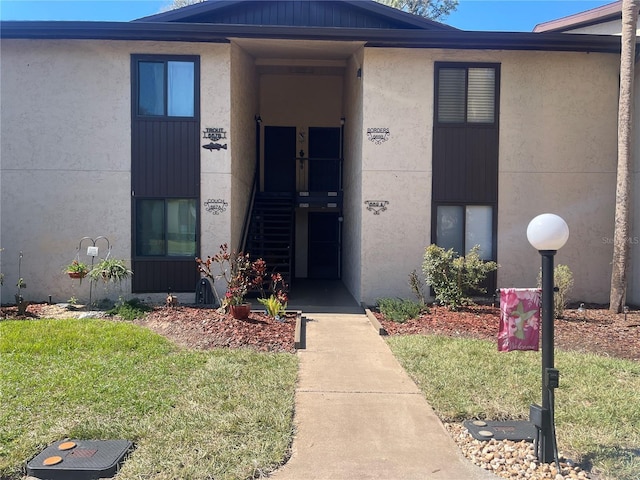 view of exterior entry featuring a lawn and stucco siding