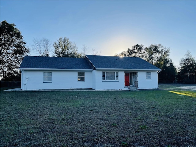 view of front of home with entry steps, roof with shingles, fence, and a lawn