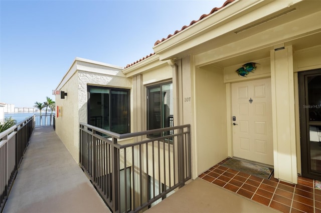 view of exterior entry with a tile roof, a balcony, and stucco siding