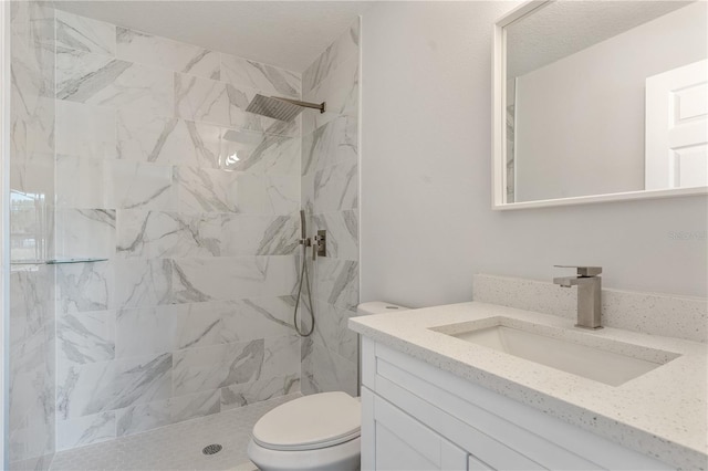 bathroom featuring vanity, a tile shower, and toilet