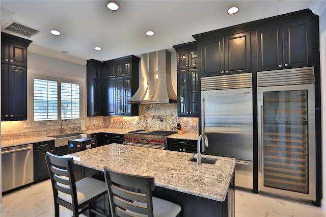 kitchen with sink, beverage cooler, premium appliances, wall chimney range hood, and a center island with sink