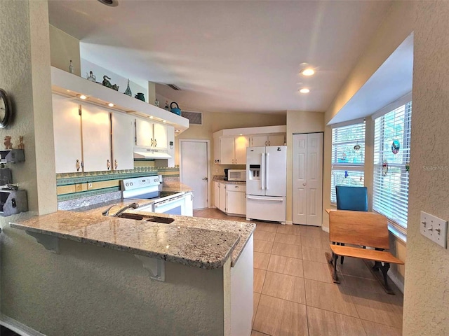 kitchen with white appliances, white cabinetry, light stone countertops, light tile patterned flooring, and kitchen peninsula