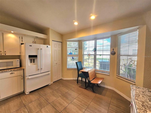 kitchen featuring light stone counters, white appliances, white cabinetry, and light tile patterned floors