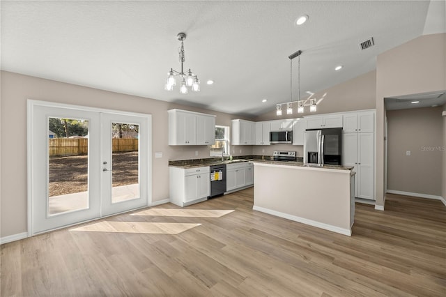 kitchen with appliances with stainless steel finishes, white cabinetry, hanging light fixtures, a center island, and vaulted ceiling